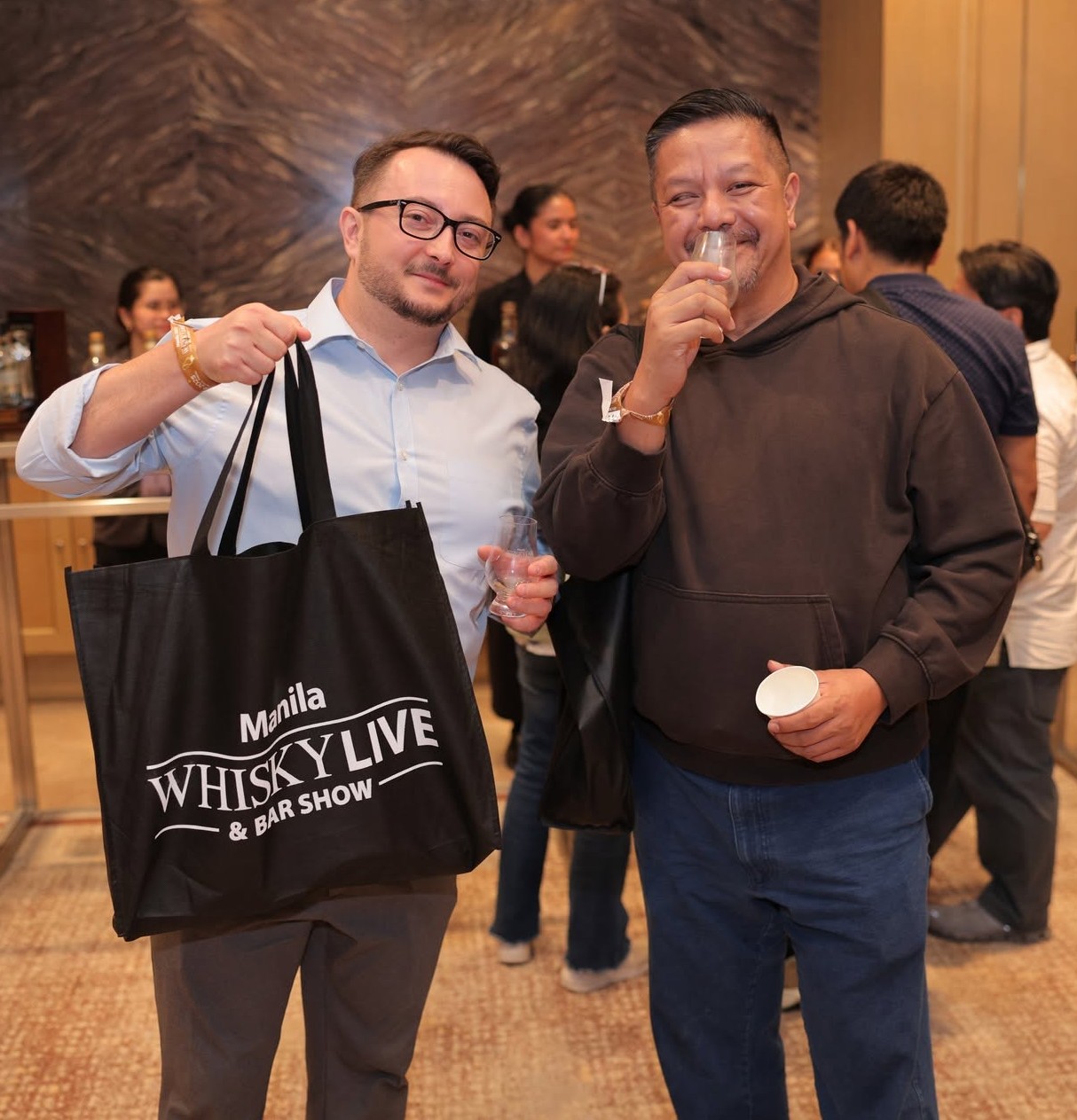 A guest holding a Whisky Live tote bag while another tastes a dram